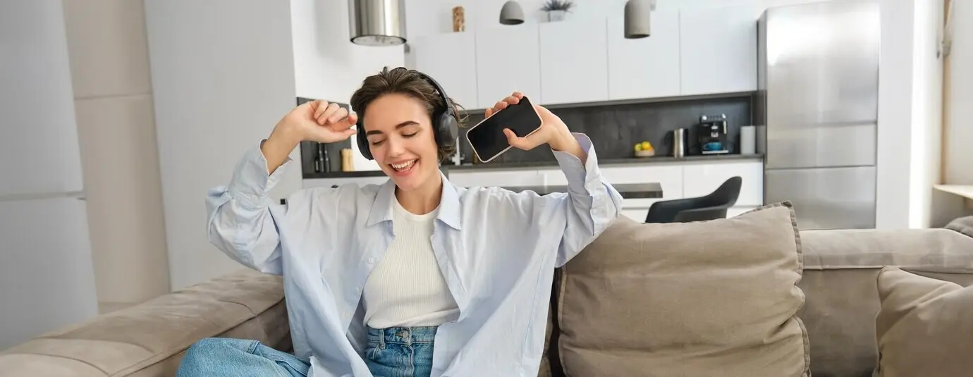 Portret van een mooie, gelukkige jonge vrouw die met een koptelefoon op naar muziek luistert, een smartphone vasthoudt en danst.